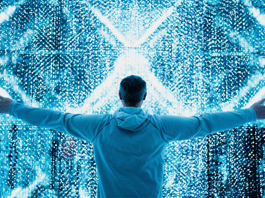 Man with outstretched arms stands in front of digital light display.