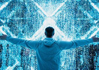 Man with outstretched arms stands in front of digital light display.