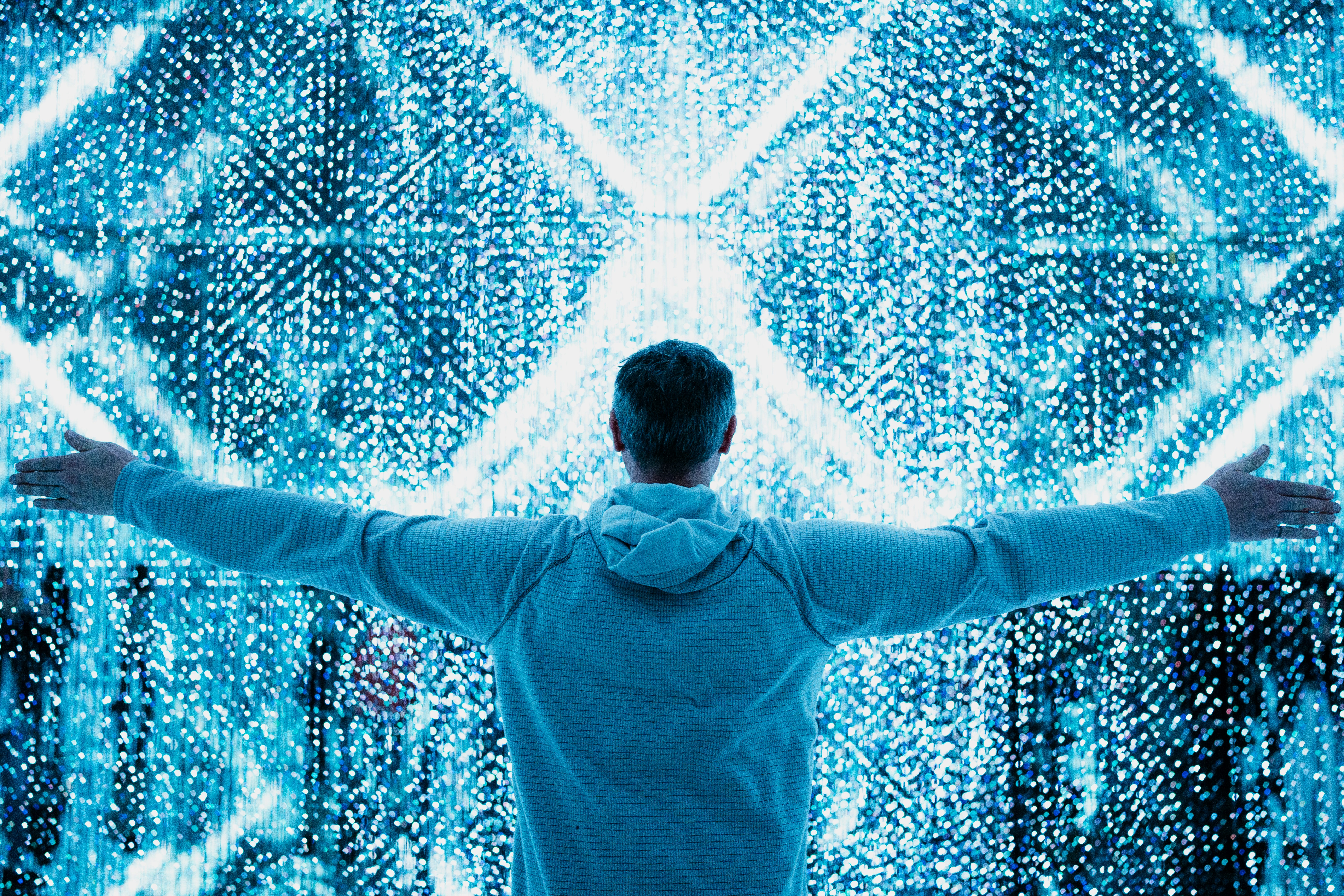 Man with outstretched arms stands in front of digital light display.