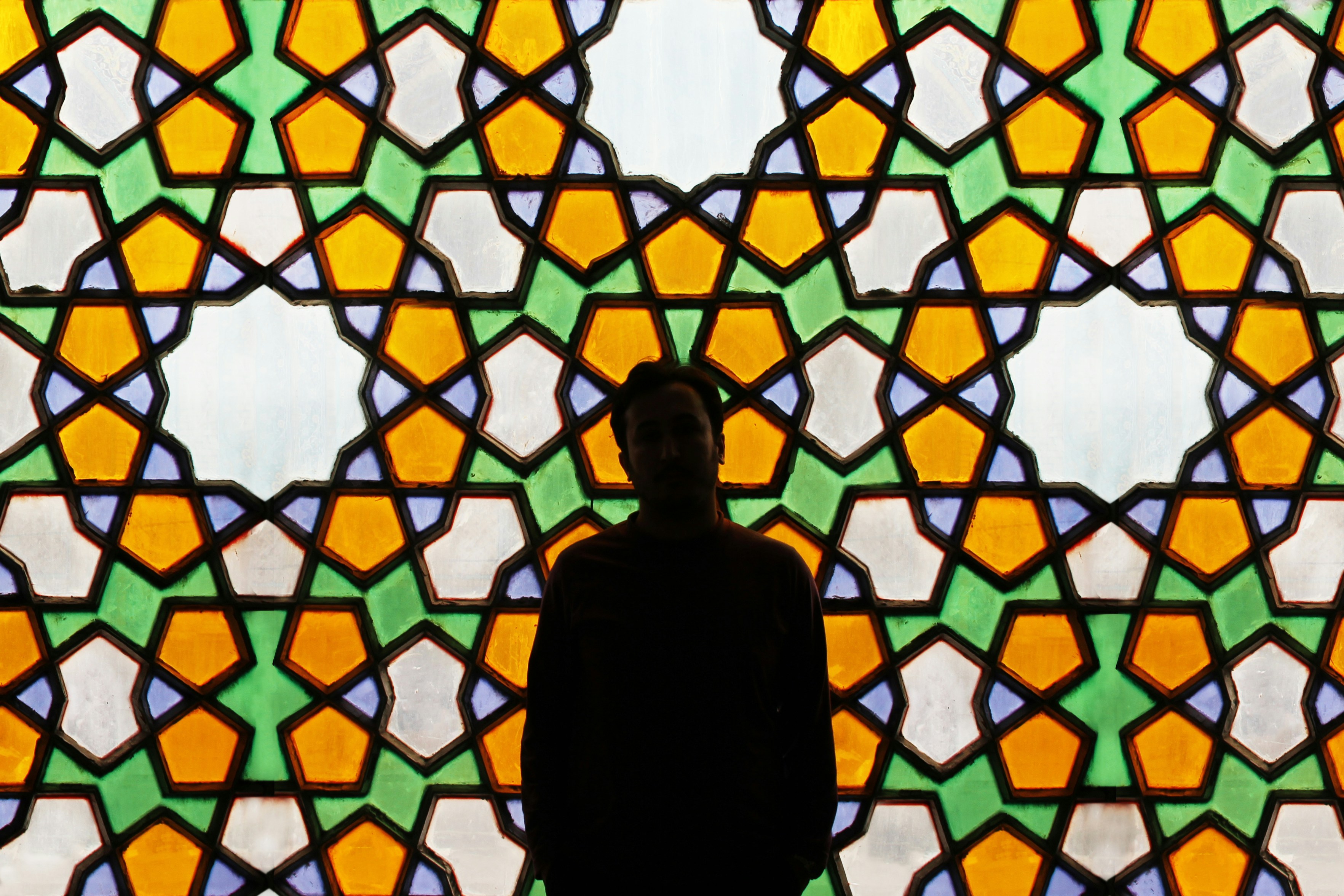 A man standing in front of a Persian window.